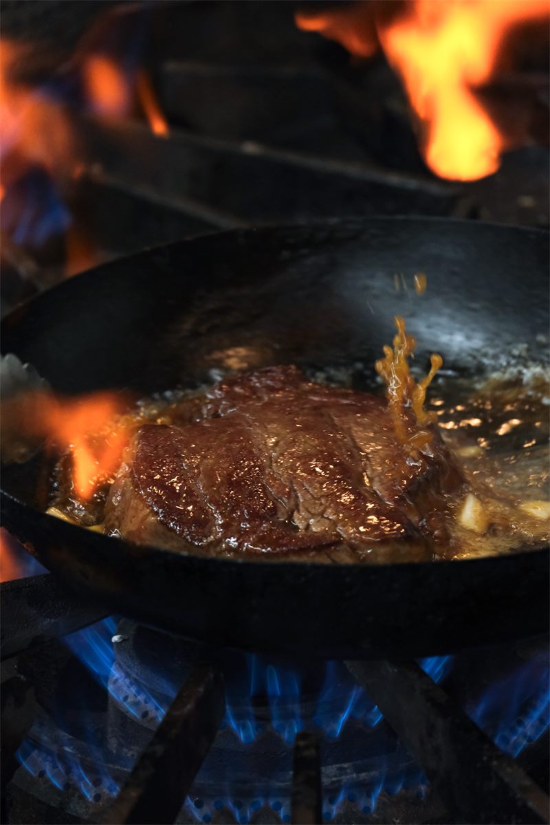 炎の立つ鍋で肉を焼きあげる